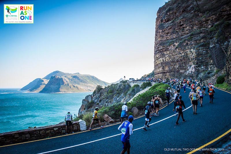 Corredores en el Maratón de los Dos Océanos, Sudáfrica, con vistas costeras y ambiente épico.